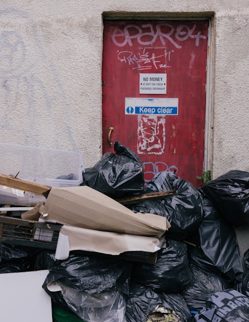 A collection of discarded items placed on a paved outdoor surface, including a wooden garden chair with slatted legs leaning against a wall, a broken white cabinet with its door removed and debris spi