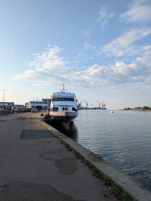 The image depicts two passenger ferries docked at a marina, with a clear view of their modern, white hulls accented by yellow stripes along the lower sections. The ferry on the left displays a namepla